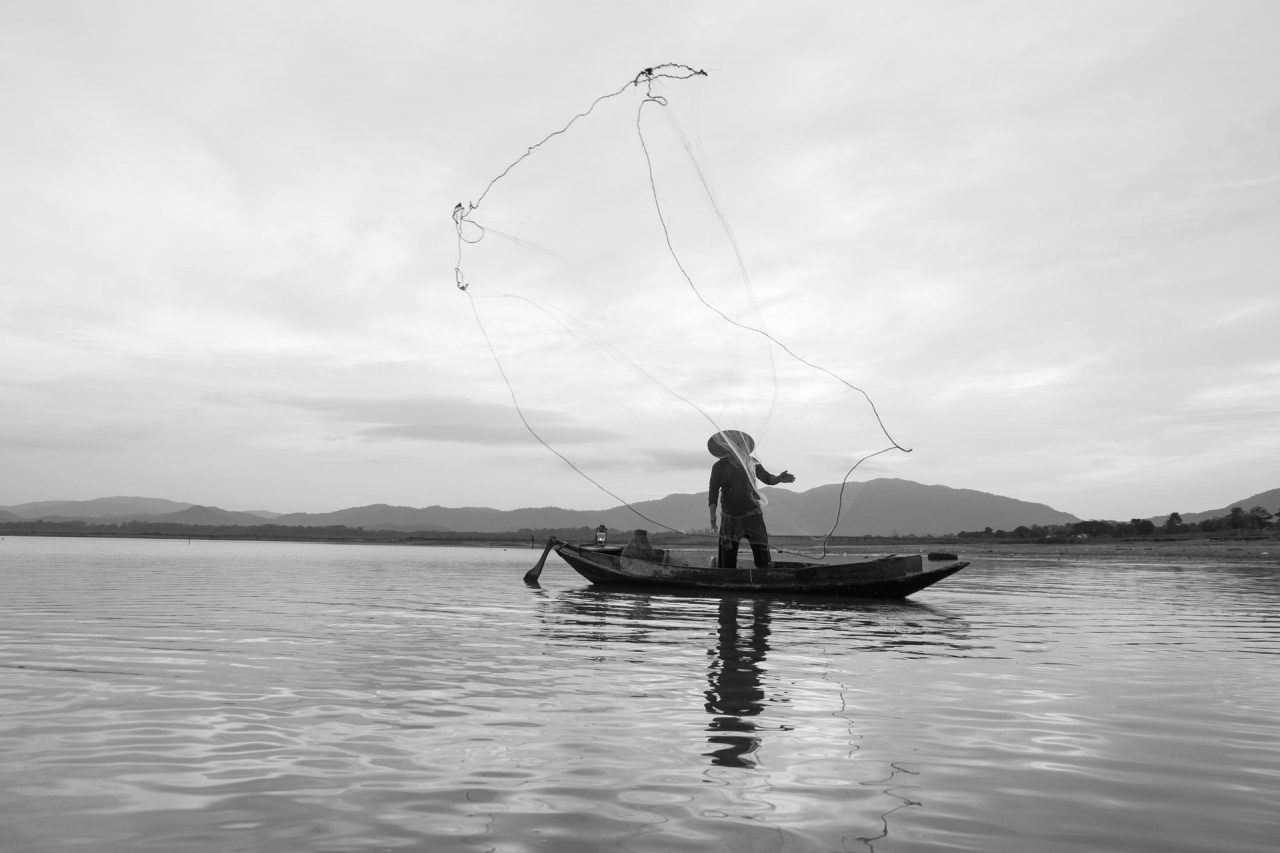 Native man fishing with net on his boat in a lake