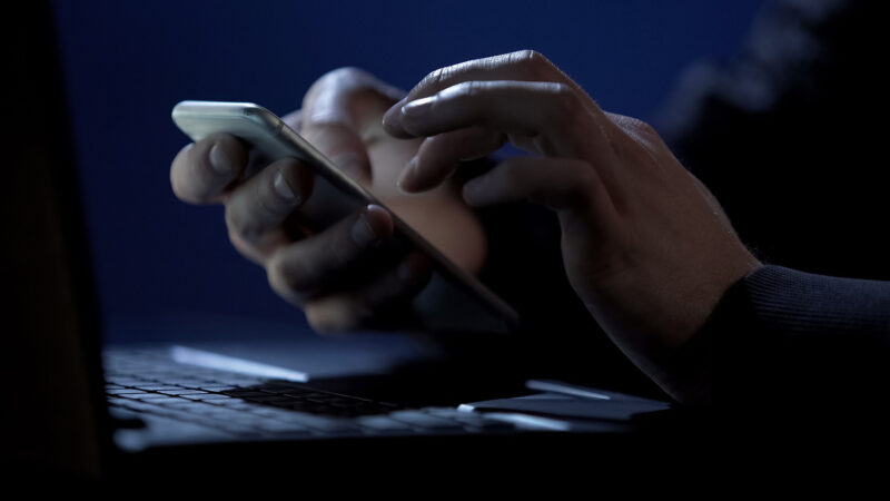 Scammer holding smartphone in a dark room